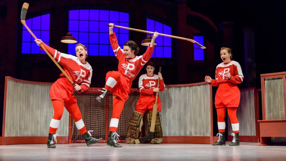 Quatre jeunes filles en uniforme de hockey sautent de joie sur une patinoire.
