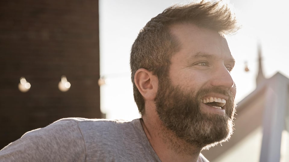 Un homme regardant vers la droite, souriant, devant un paysage urbain.