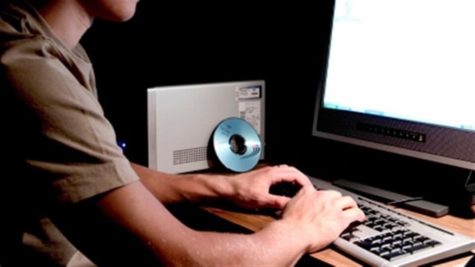 Une personne pianote sur un clavier d'ordinateur dans une pièce sombre.