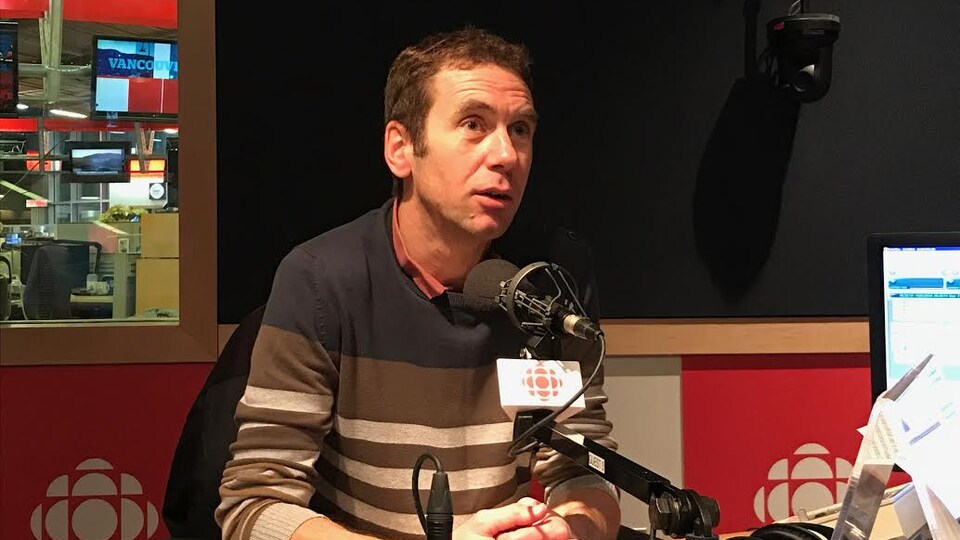 Un homme est assis devant un micro, dans un un studio radio.