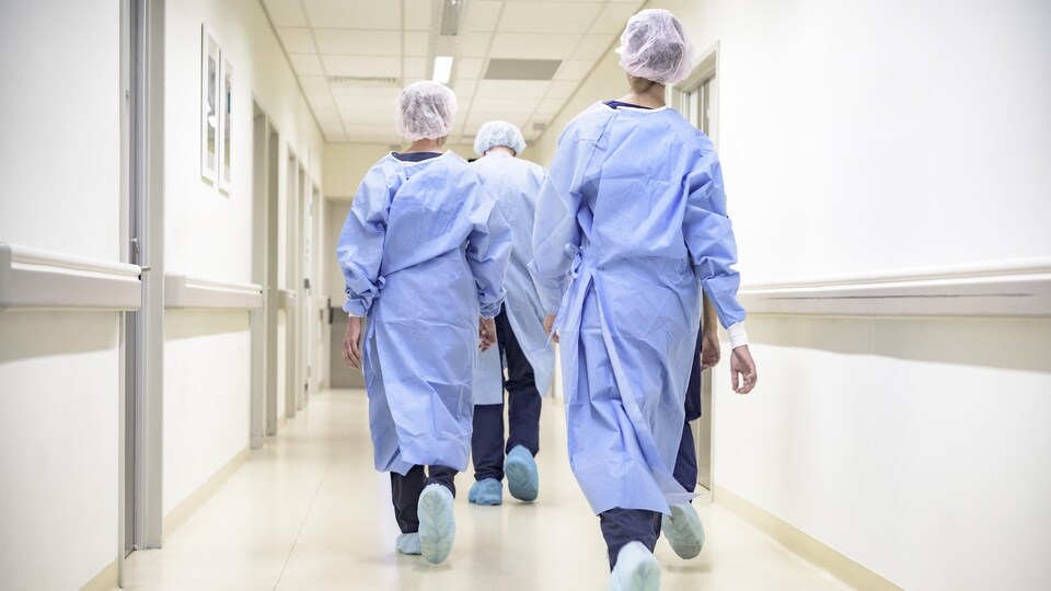 Des infirmières, vues de dos, marchent dans le corridor d'un hôpital.