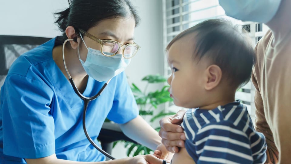 Une femme qui porte des lunettes examine un bébé avec un stéthoscope.