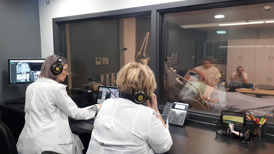 Enseignants en soins infirmiers derrière une console qui supervisent des étudiants en train de pratiquer des interventions sur un mannequin.