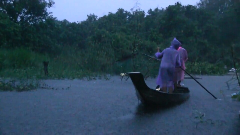 2 personnes sont dans un canot qui flotte sur un paysage inondé.
