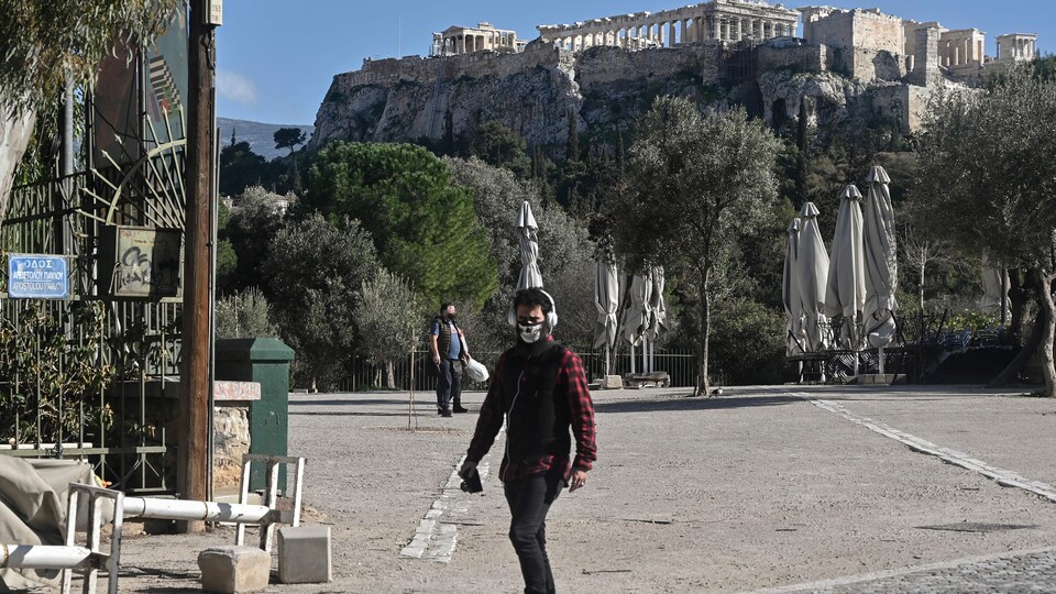 Une personne masquée marche au pied de l'Acropole à Athènes. 