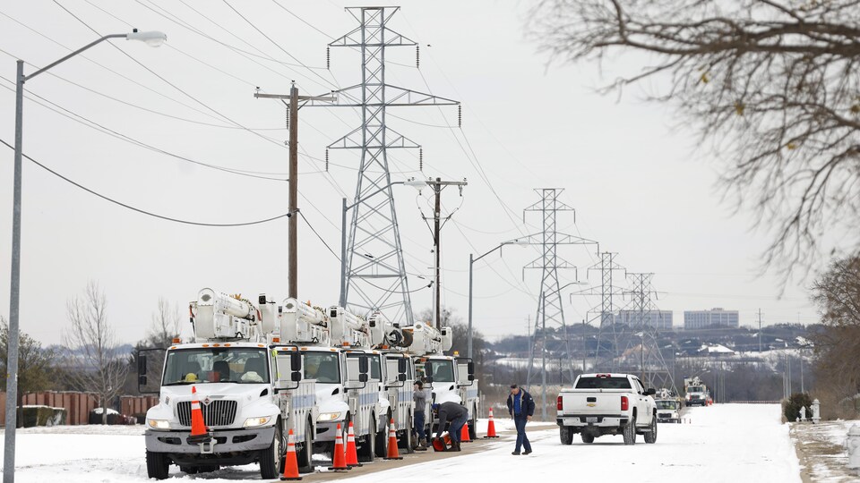 Des monteurs de ligne près de leurs camions aux abords de pylônes électriques en hiver.