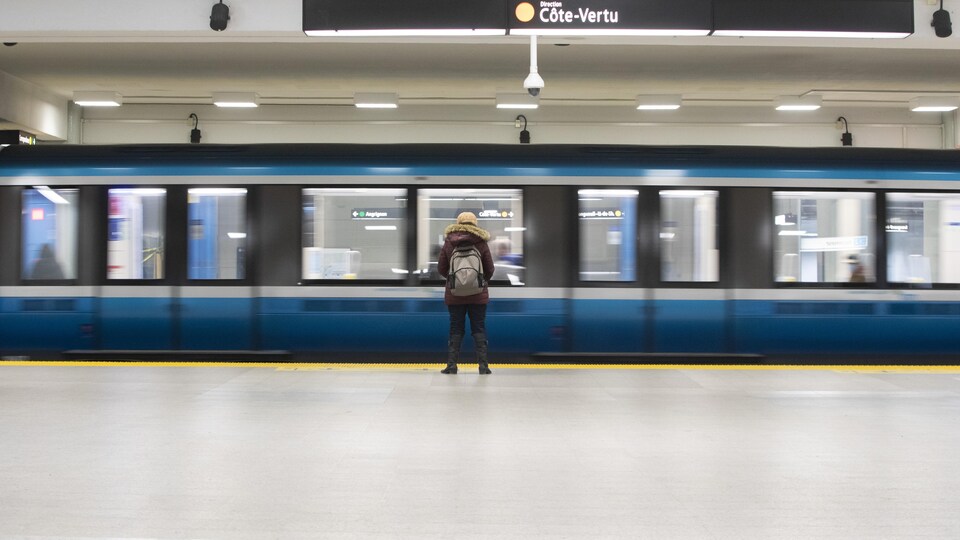 Une personne attend sur le quai de la ligne orange alors que le métro s'immobilise sur les rails.