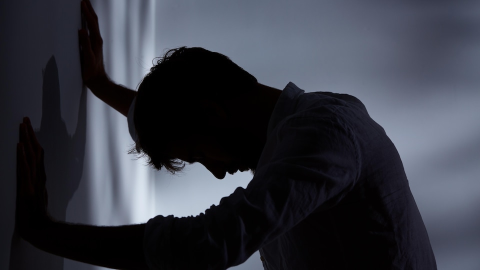 Un homme appuyé sur un mur dans une pièce sombre.