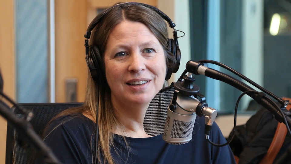 Une femme avec des écouteurs sur la tête parle dans un micro dans un studio de radio. 