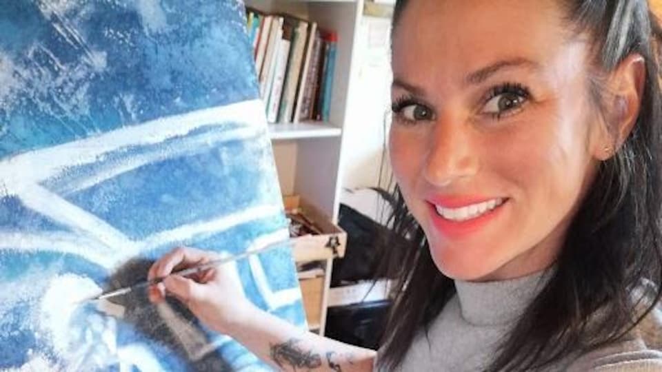 Isabelle Turbide sourit, un pinceau à la main, devant sa toile.