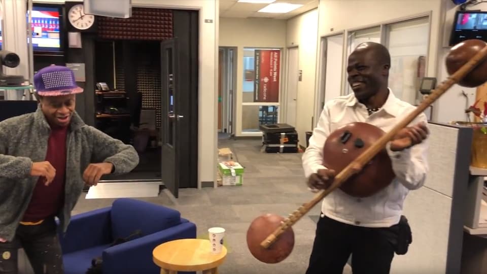 deux africains blacks dans les bureaux de Radio-Canada à Victoria un à casquette et qui danse, l,autre aqui souriant en jouant d'un instrument traditionel à cordes et calebasses.