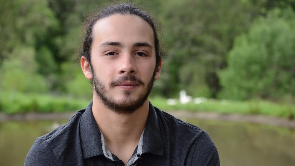 Un jeune homme est photographié en avant-plan d'un étang