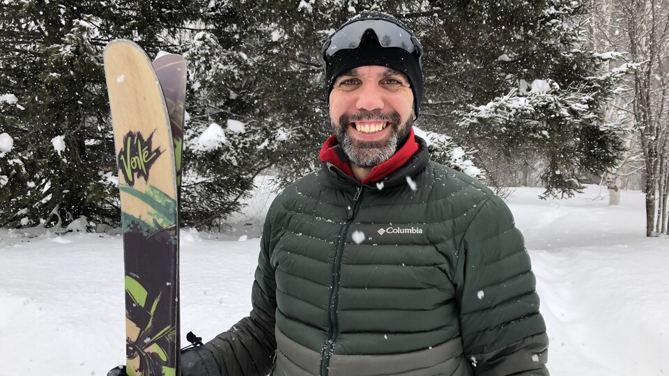 Jacob Racine pose avec ses skis, devant un paysage enneigé.
