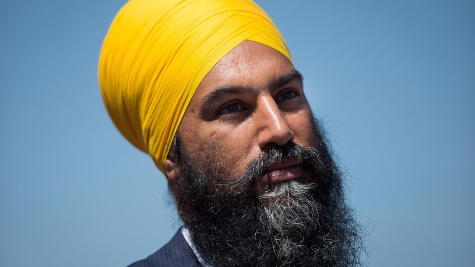 Un homme avec un turban jaune est photographié plan épaule sur fond bleu.
