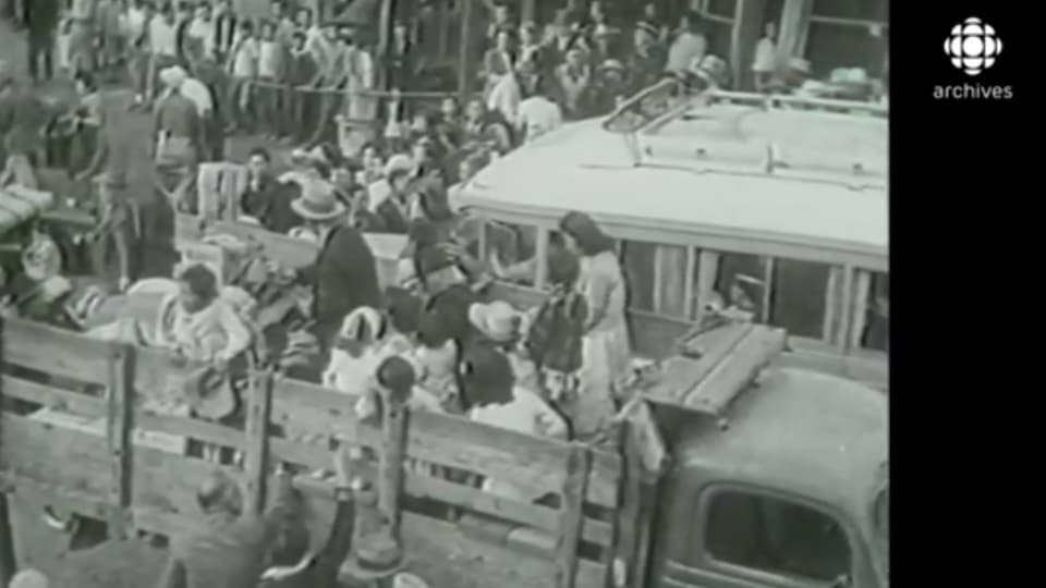 Scène en noir et blanc des familles de Canadiens d'origine japonaise entassées dans des camions.