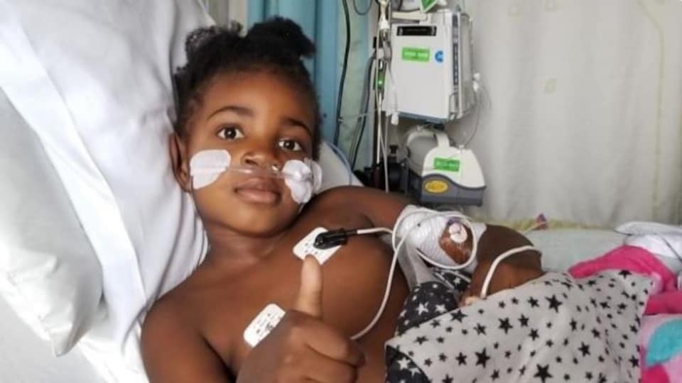 Une petite fille dans son lit d'hôpital fait signe de bien aller avec un pouce levé vers le haut.