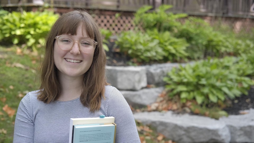Portrait de Dominique à l'extérieur. Elle tient deux livres dans ses mains.