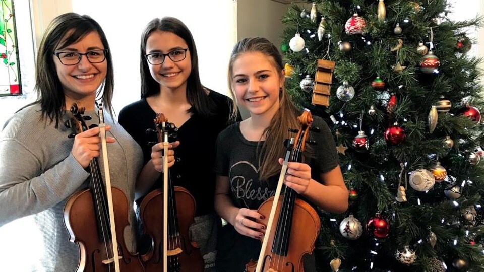 Elles se tiennent debout devant leur sapin de Noël tenant un violon.