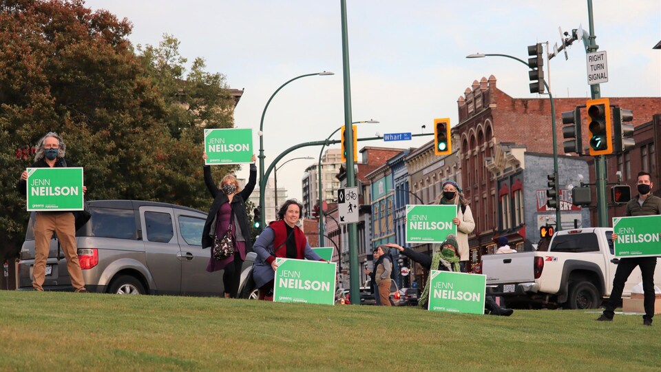 Jenn Neilson est entourée de son équipe et brandit une affiche verte avec son nom.