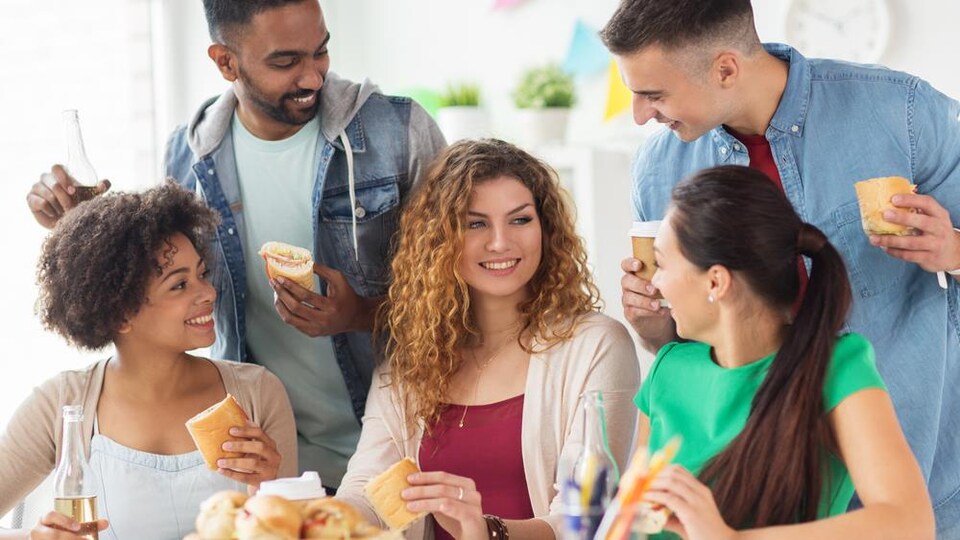 Cinq jeunes adultes discutent et mangent ensemble.