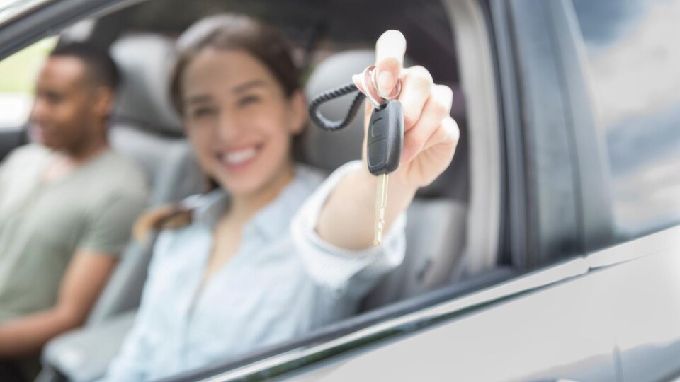 Une jeune conductrice souriante assise au volant d'une voiture montre sa clé d'auto.3567