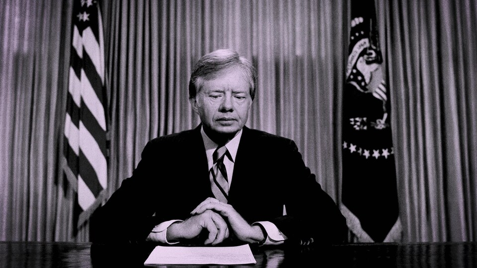 Jimmy Carter assis à un bureau, lit un texte sur une feuille.