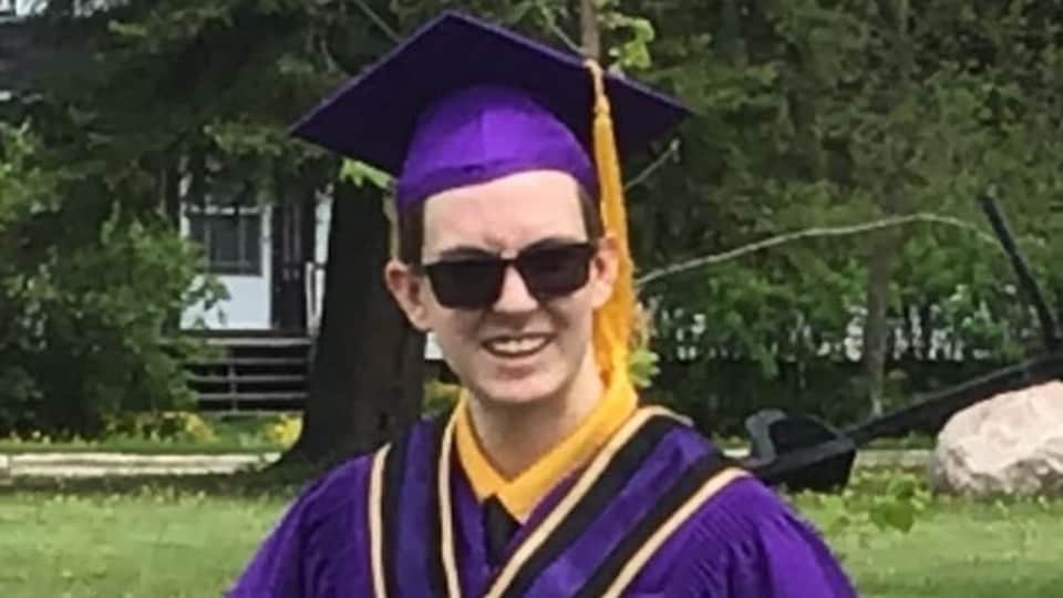 Un jeune finissant en toge de graduation tient un diplome.