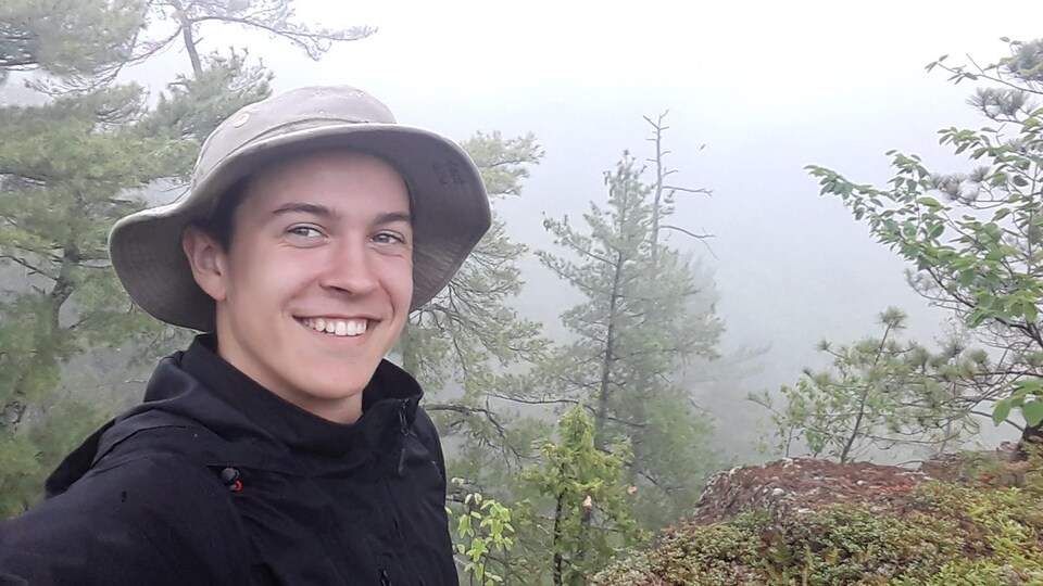 Un jeune homme souriant devant une forêt couverte de brouillard.