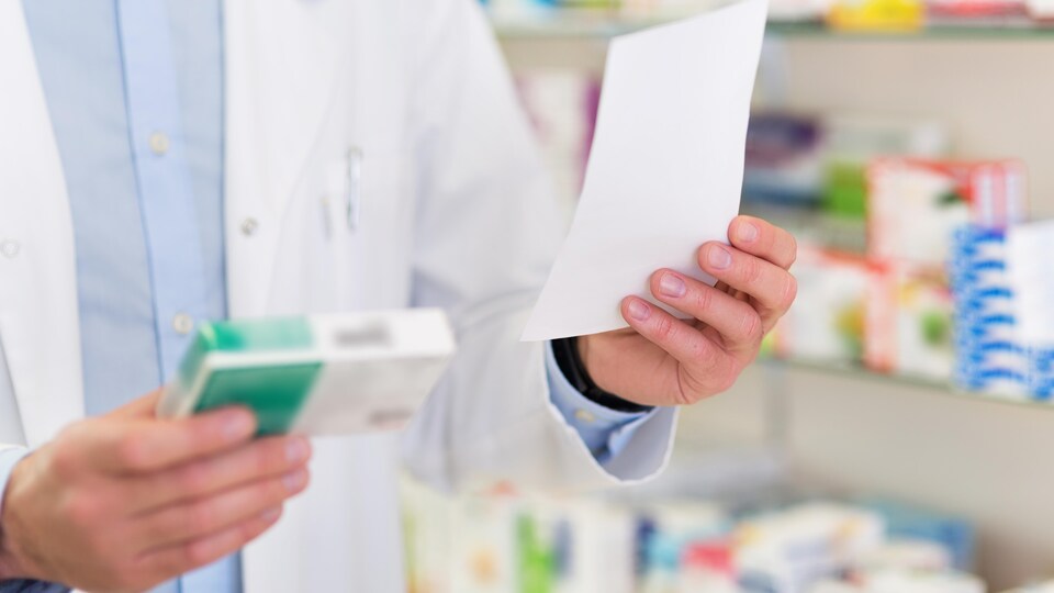 Un pharmacien tient dans une main une boîte de médicaments et dans l'autre une prescription.