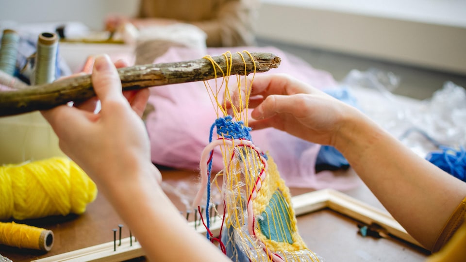Des mains de femmes en train de créer une œuvre avec des films de laine colorés.