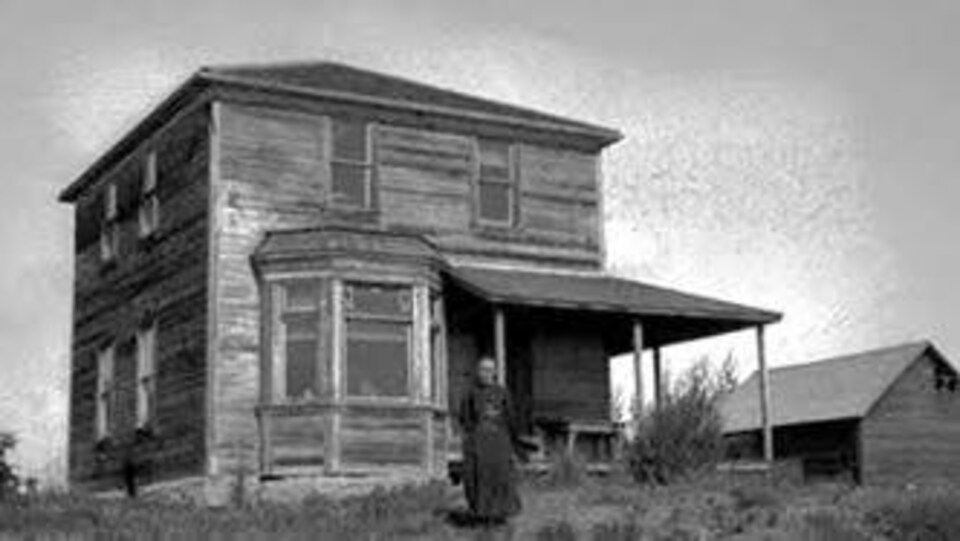 Photo noir et blanch d'une maison en bois, une femme à l'avant.