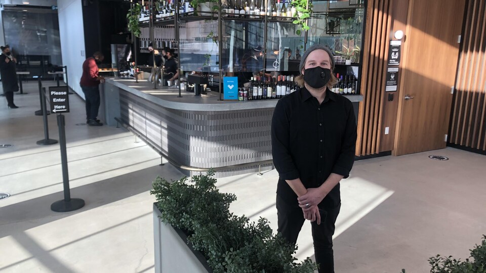 Un homme qui porte un masque se tient debout devant le bar d'un restaurant spacieux et bien éclairé.