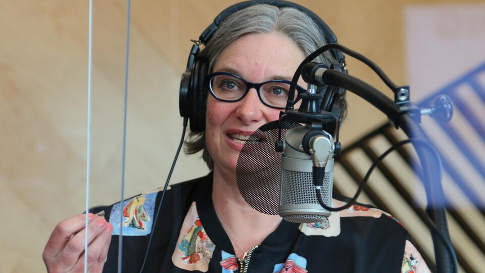 La journaliste, casque d'écoute sur la tête, parle en tenant rassemblé le bout des doigts de sa main droite, dans le Studio 1 de la nouvelle Maison de Radio-Canada. 