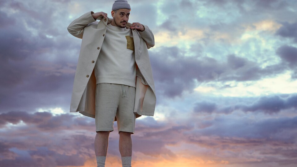 Un homme réajuste le col de son manteau avec en arrière-plan le coucher du soleil.