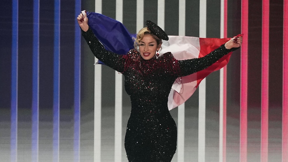 Une femme vêtue d'une robe à paillettes étincelante porte un drapeau de la France à bout de bras lors de son entrée sur scène. 