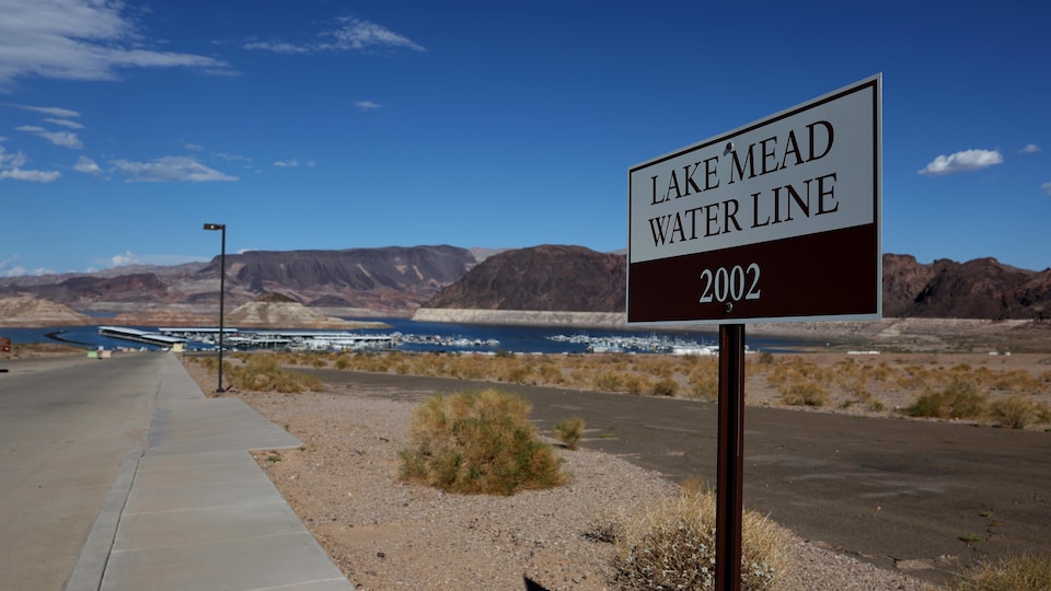 Un panneau indiquant où se trouvaient les niveaux d'eau du lac Mead en 2002 est affiché près de la marina du lac Mead. Des montagnes, du sable et des plantes qui poussent en milieu aride complètent le paysage. 
