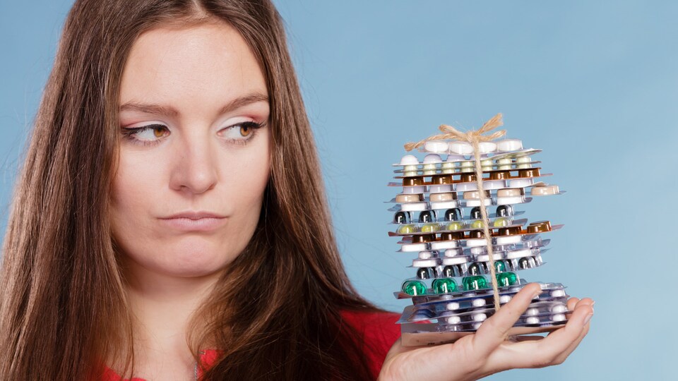 Femme tenant dans sa main de nombreux paquets qui contiennent des médicaments.