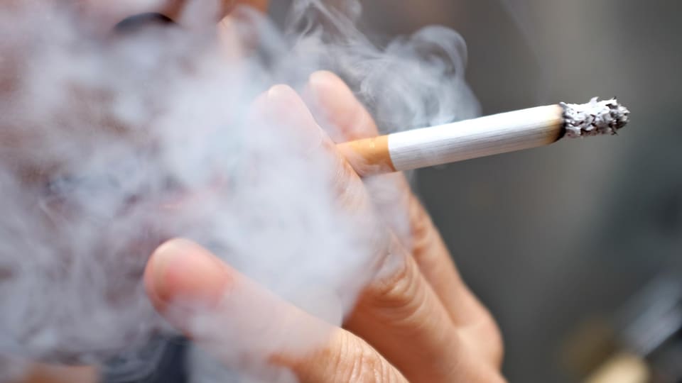 Plan rapproché de la main d'un fumeur tenant une cigarette allumée.