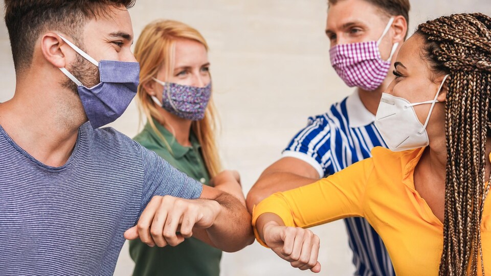 Quatre jeunes personnes masqués se saluent en touchant leur coude.