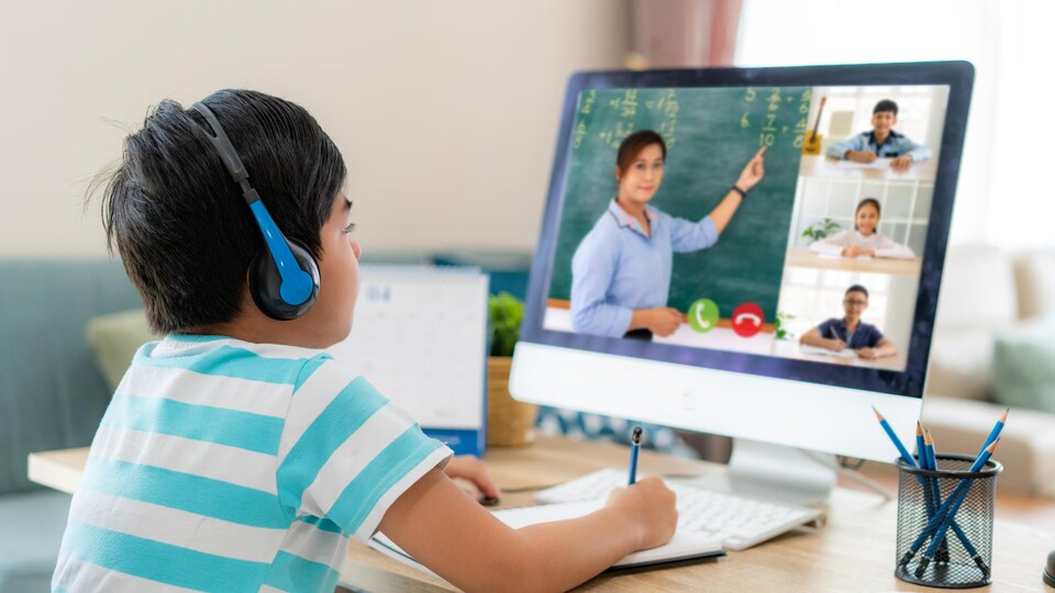 Un garçon devant un ordinateur assiste au cours donné par sa professeure.