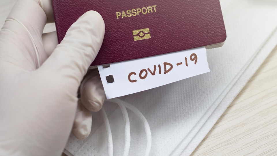 Une main tient un passeport duquel sort une fiche avec le mot COVID-19.