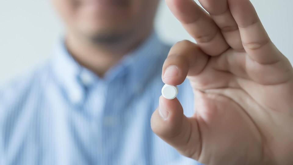 Un homme tient une pilule entre ses doigts à bout de bras.