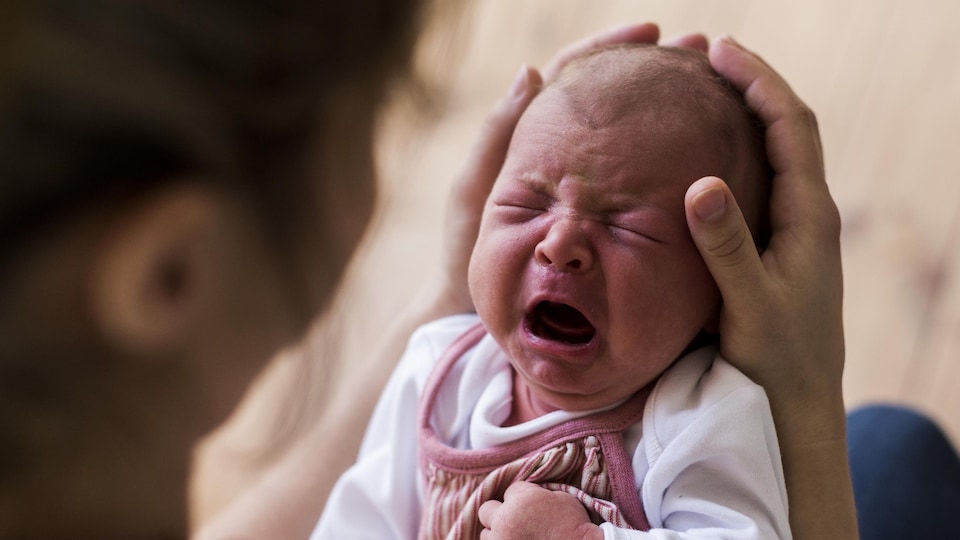 Un bébé qui pleure dans les bras de sa mère. 
