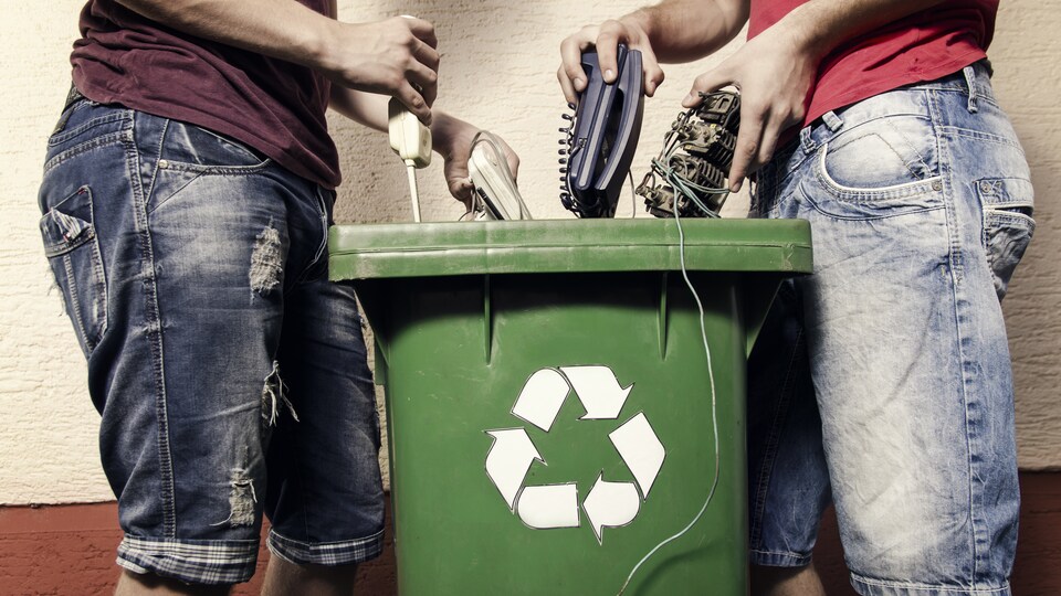 Deux homme jettent des déchets électroniques dans un bac de recyclage.