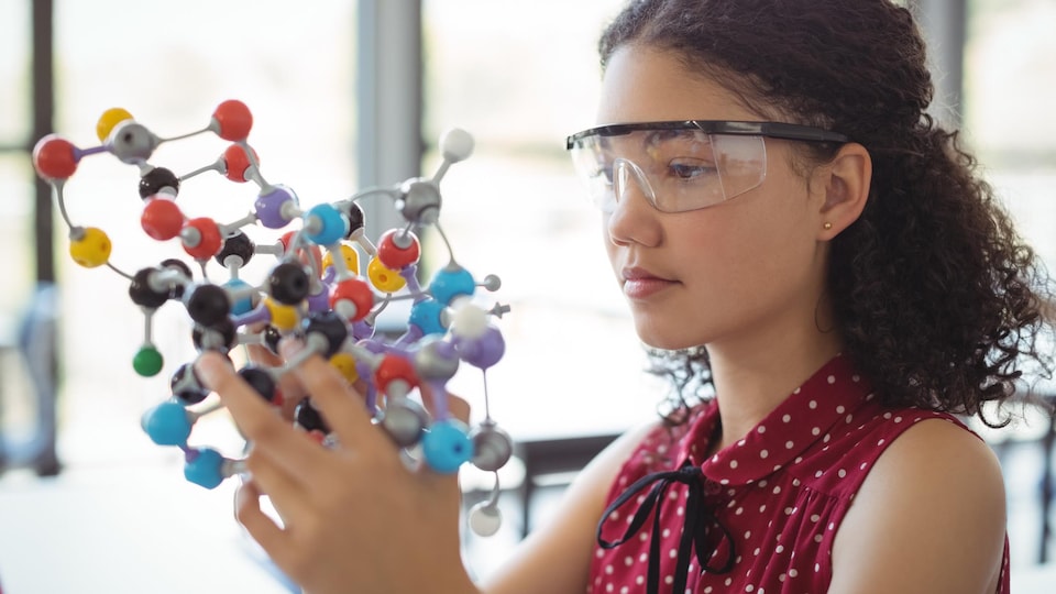 Une jeune femme tient un modèle de molécule dans ses mains.