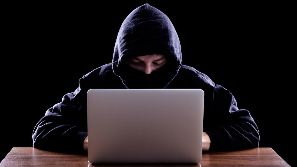 Une jeune homme devant son ordinateur portable, avec un bandeau qui cache son visage. 