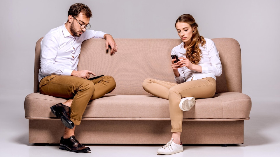 Jeune couple qui texte, assis sur un divan. 