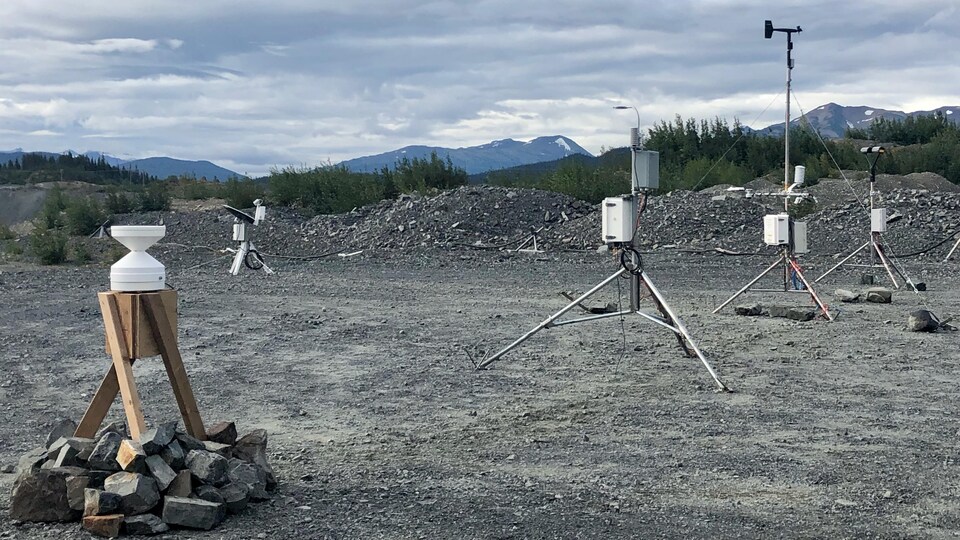 Divers instruments de mesure scientifiques sont posés sur des trépieds, à quelques mètres les uns des autres, sur un site extérieur recouvert de gravier, qui semble désaffecté.