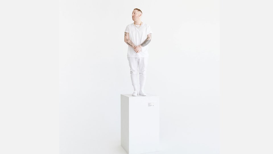 Un homme tout en blanc se tient sur un socle blanc dans un décor immaculé.