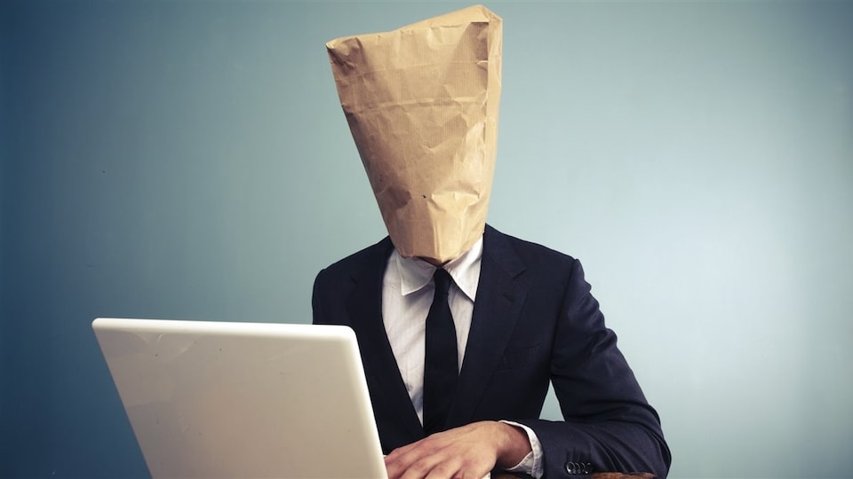 Un homme dont la tête est enfouie sous un sac de papier brun consulte l'Internet sur son ordinateur portable.